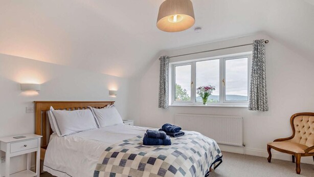 A bedroom with a bed, bedside tables, a chair, a window with curtains, and a hanging light fixture. - 3 Bed in Ross-on-wye (oc-89313) (Bridstow)
