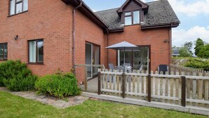 A brick house with a patio, a wooden fence, and a clear sky. - 3 Bed in Ross-on-wye (oc-89313) (Bridstow)