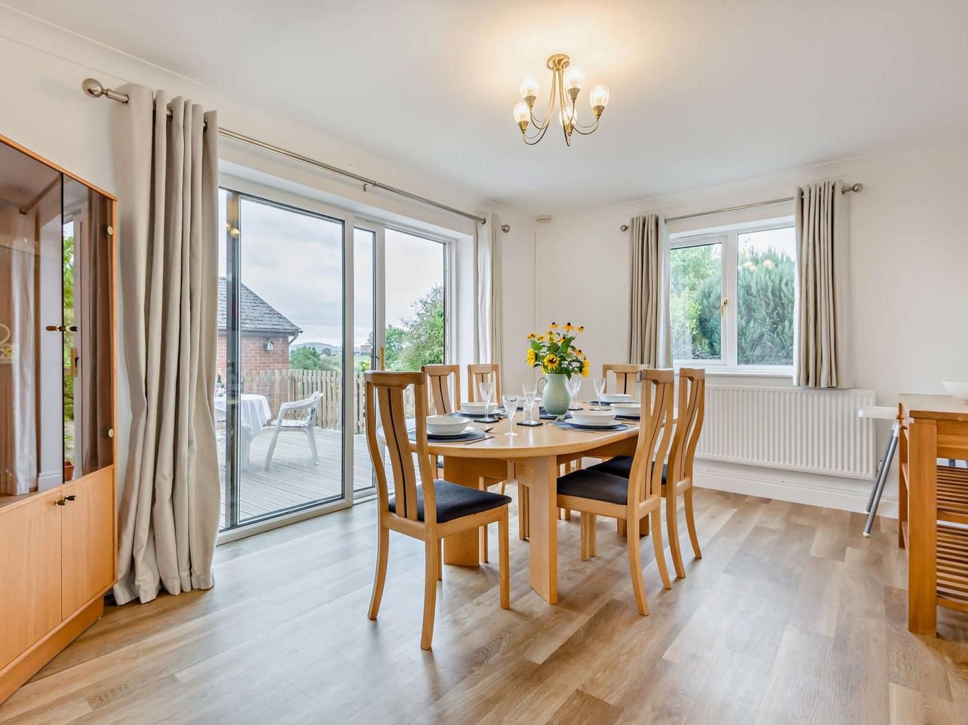 Un coin repas avec une table dressée pour quatre personnes, des chaises en bois, un vase rempli de fleurs et une vue dégagée grâce à de grandes fenêtres.