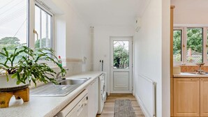 A narrow kitchen with a built-in dishwasher, a sink, and a window overlooking a garden. - 3 Bed in Ross-on-wye (oc-89313) (Bridstow)
