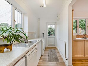 Eine schmale Küche mit eingebautem Geschirrspüler, Spüle und Fenster mit Blick auf einen Garten.