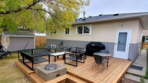 Ein Garten mit einer Holzterrasse, Gartenmöbeln, einem Grill und einem Geräteschuppen.