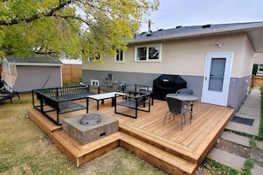 Ein Garten mit einer Holzterrasse, Gartenmöbeln, einem Grill und einem Geräteschuppen.