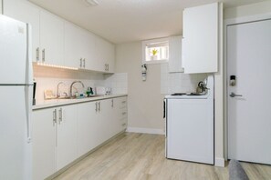 Ett kompakt kök med vita skåp, en inbyggd ugn och ett fönster ovanför diskbänken.