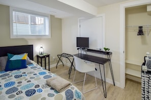 Ein Schlafzimmer mit Bett, Schreibtisch, Stuhl, Fernseher und einem Fenster mit Jalousien.