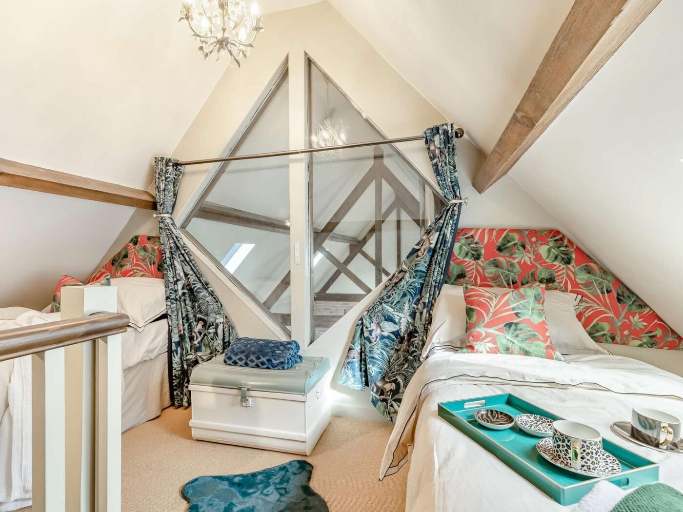 Une chambre à coucher avec un lit, une valise, un plateau avec des tasses et des soucoupes, et un fauteuil suspendu.