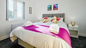 Een slaapkamer met een bed, een raam, een nachtkastje en een lamp.