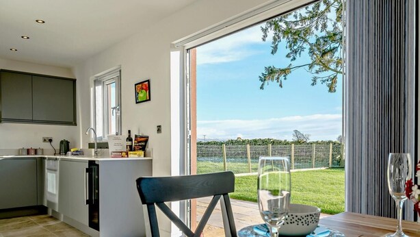 Een moderne keuken met een eiland, een eethoek met een tafel voor twee en een grote schuifdeur naar een gazon.