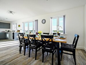Een moderne eetruimte met een houten tafel en zwarte stoelen, een keuken op de achtergrond en grote ramen met uitzicht.