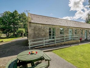 A stone building with a tiled roof, a small porch with a railing, and a picnic table with food and drinks. - 2 Bed in Sanquhar (oc-89403) (Sanquhar)