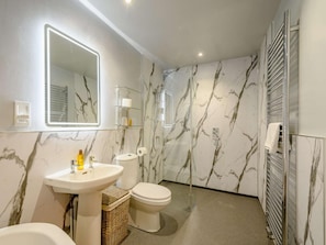 Ein Badezimmer mit Marmorwand, Waschbecken, Toilette, Spiegel und Handtuchhalter.