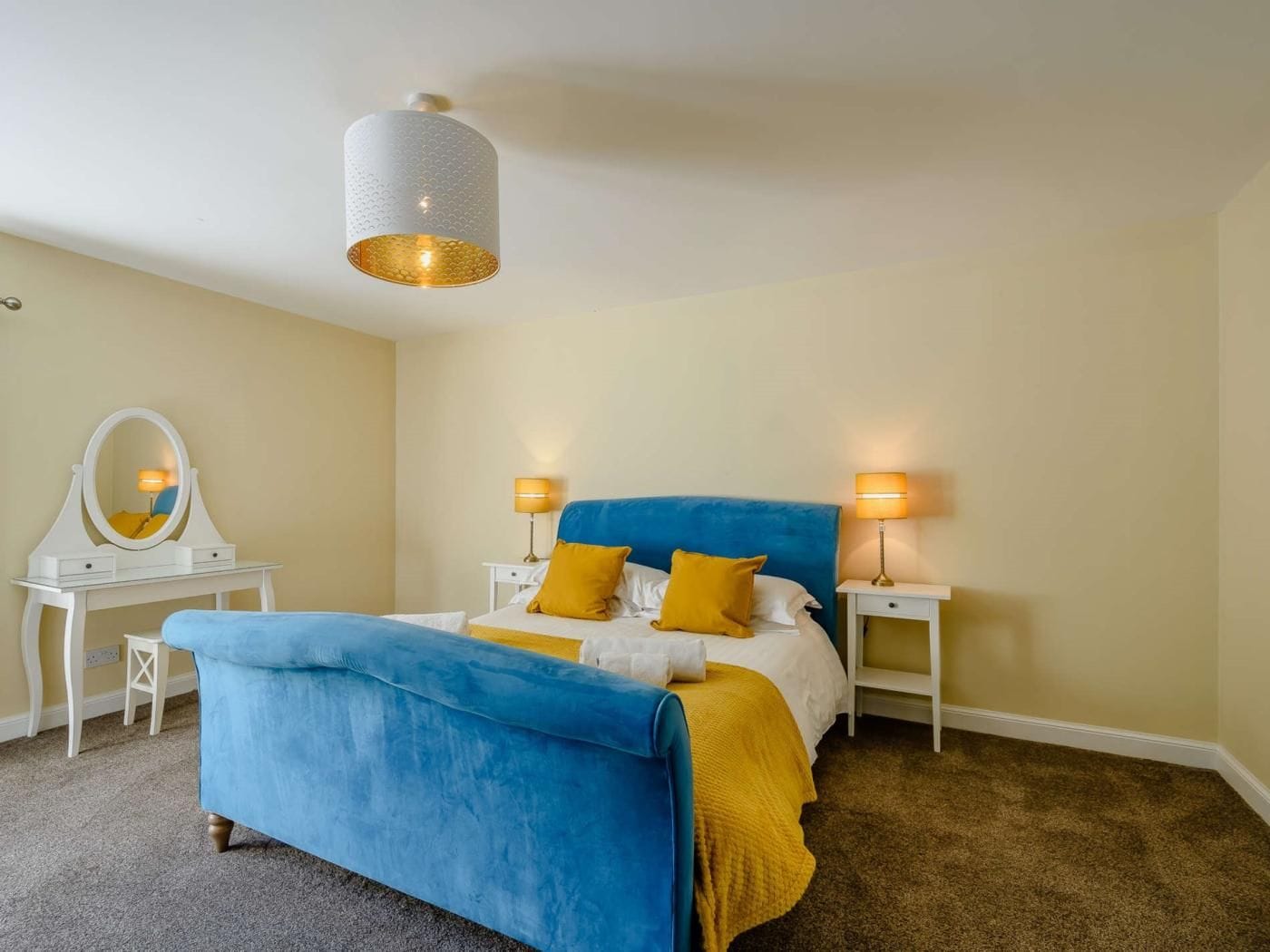 A bedroom with a bed, bedside tables, lamps, a mirror, and a hanging light fixture.