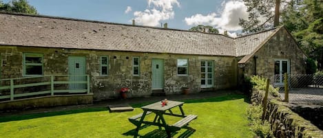Un edificio de piedra con un patio cubierto de césped, una mesa de picnic y un muro de piedra.