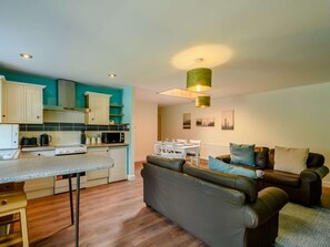 A modern kitchen with white cabinets, a dining area with a table and chairs, and a living room with a sofa and cushions. - 2 Bed in Sanquhar (oc-89402) (Sanquhar)