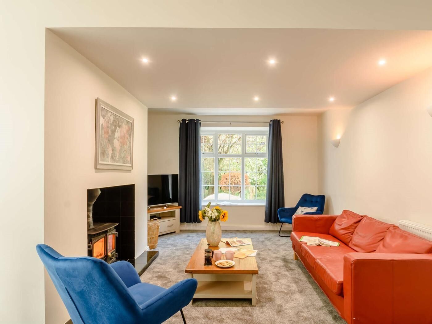 A living room with a fireplace, a sofa, a blue armchair, a coffee table, and a window with curtains.
