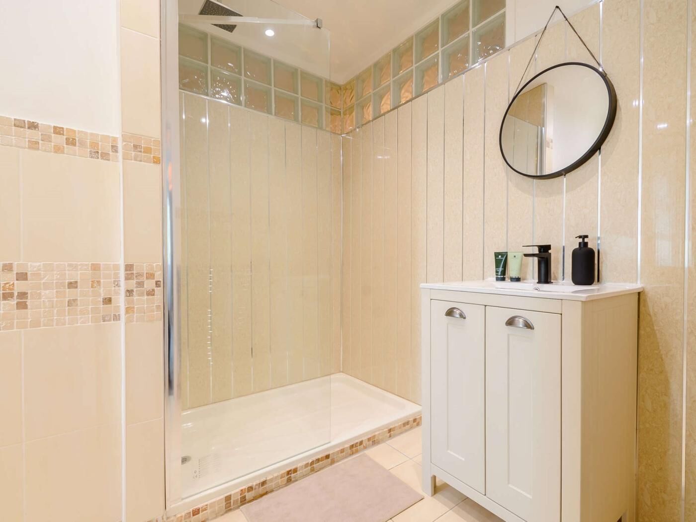 A modern bathroom with a glass-enclosed shower, a vanity with a mirror, and a tiled floor.