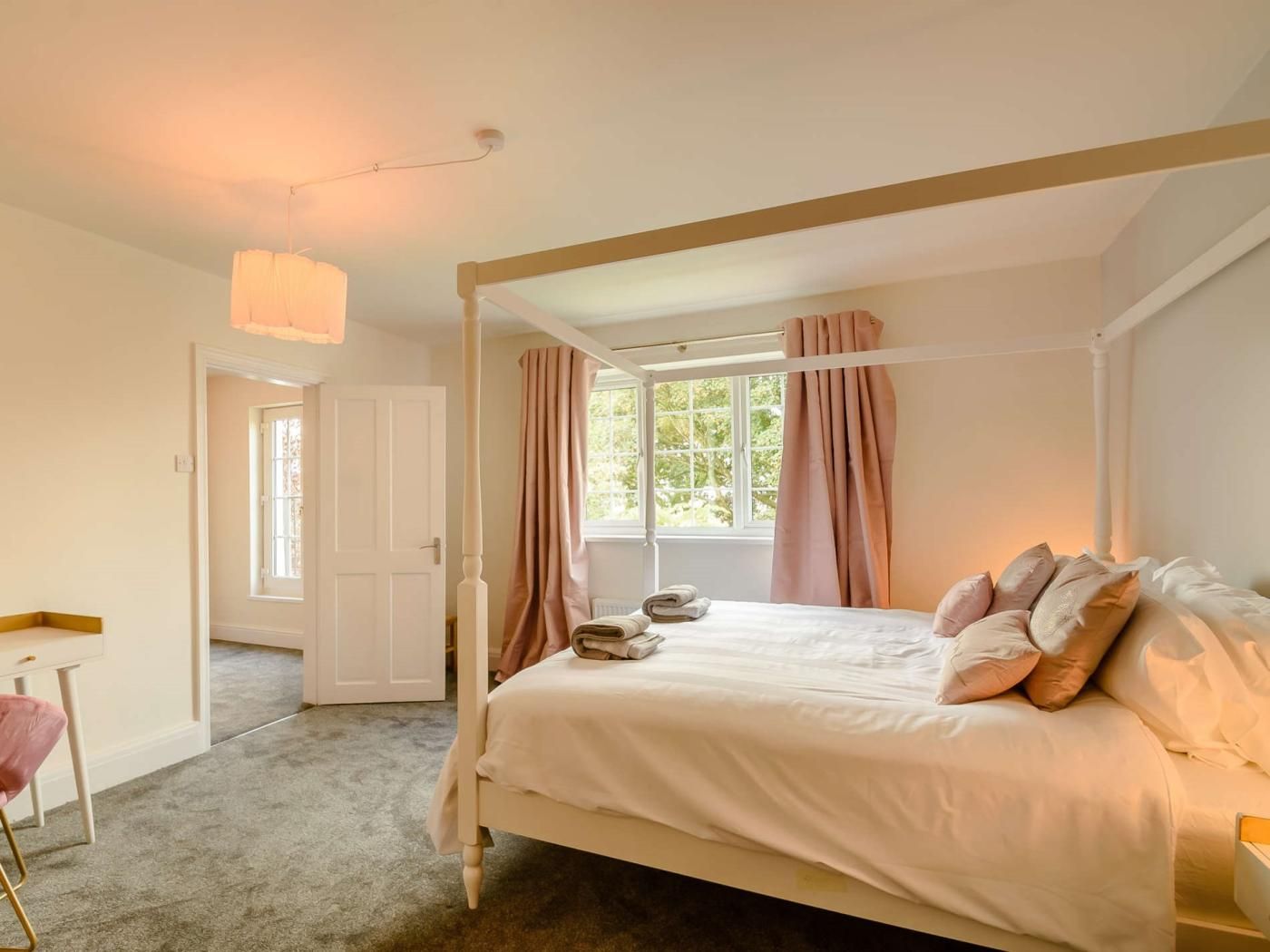 A four-poster bed with a canopy, a desk with a chair, a window with curtains, and a door.