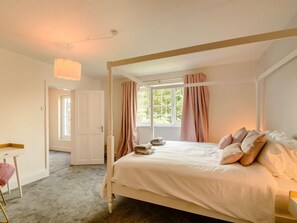 A four-poster bed with a canopy, a desk with a chair, a window with curtains, and a door.