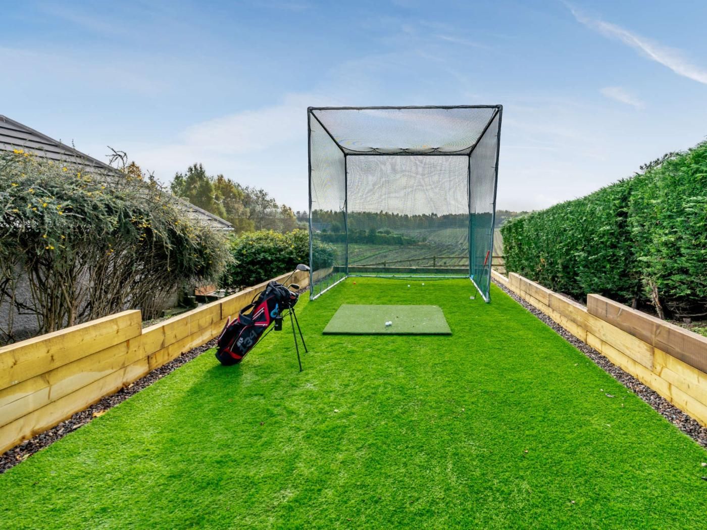 A golf practice area with a netted practice zone, a putting green, and a golf bag.