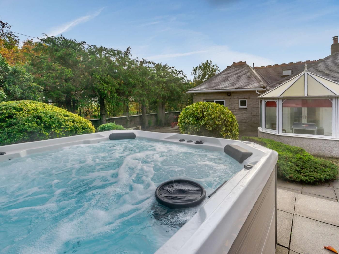 Ein Whirlpool in einem Garten mit einem Haus und Bäumen im Hintergrund.