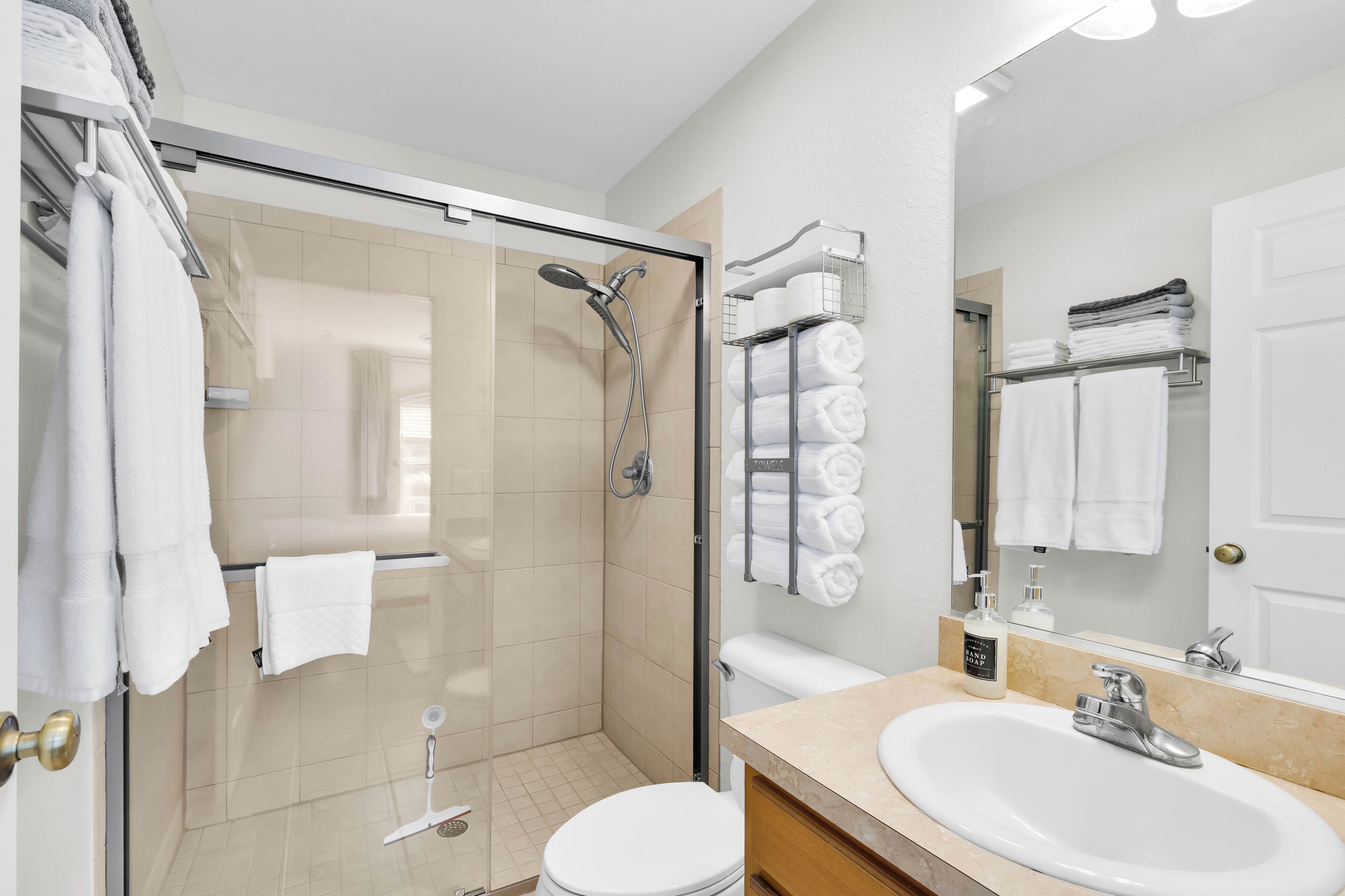 Een moderne badkamer met een douchecabine van glas, een wit toilet, een wastafel met spiegel en netjes opgevouwen handdoeken.
