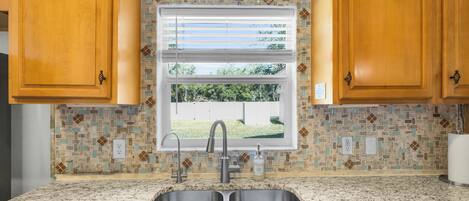 A kitchen with wooden cabinets, a double sink, a window with blinds, and a mosaic backsplash.