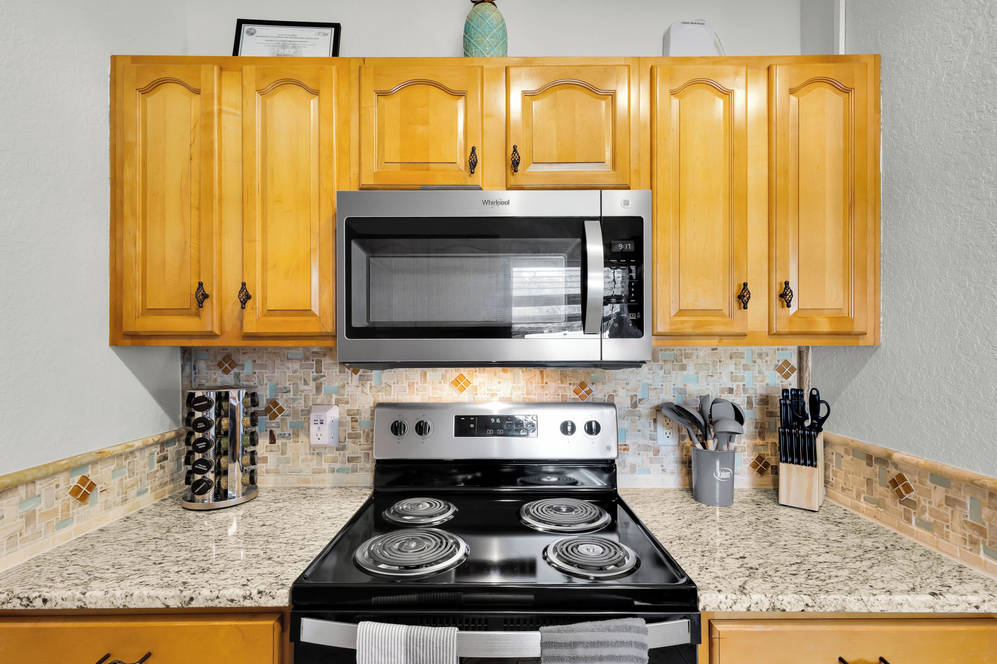 A kitchen with wooden cabinets, a stainless steel microwave, a gas stove, and a tiled backsplash.