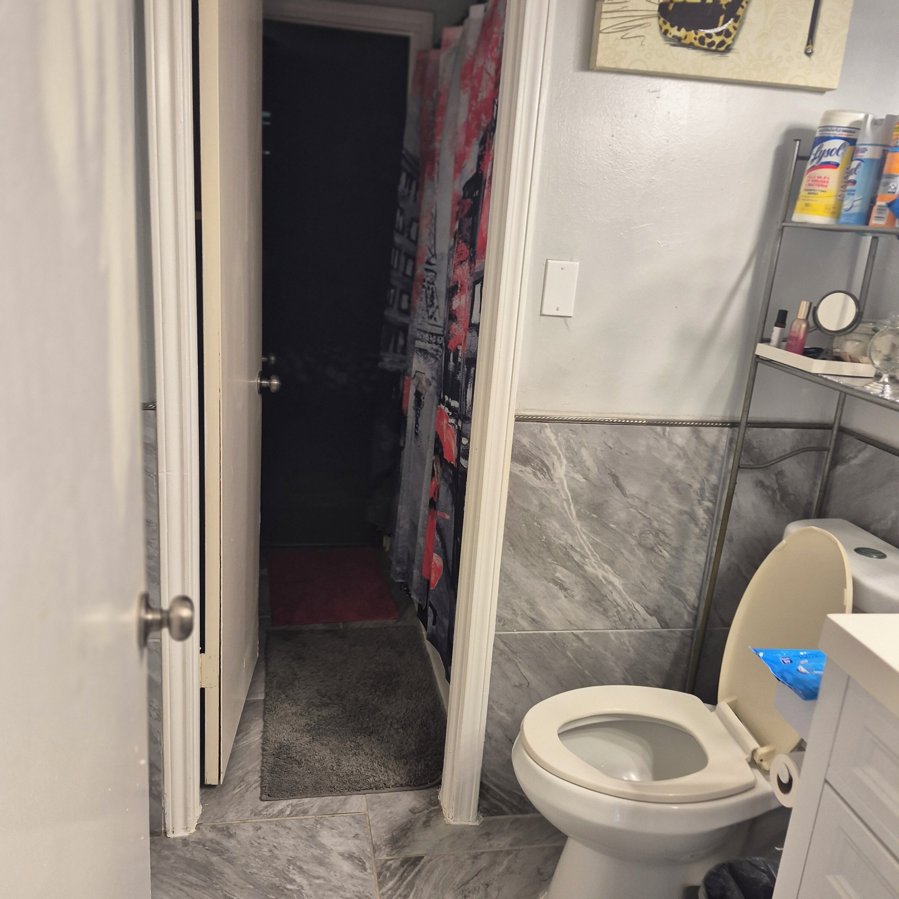A bathroom with a toilet, a shower curtain, a marble floor, and a shelf with toiletries.