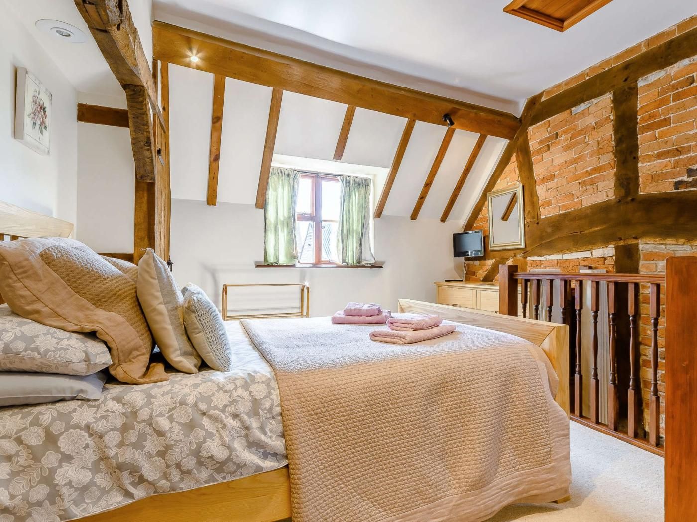 Un dormitorio con cama, ventana, televisor y pared de ladrillo.