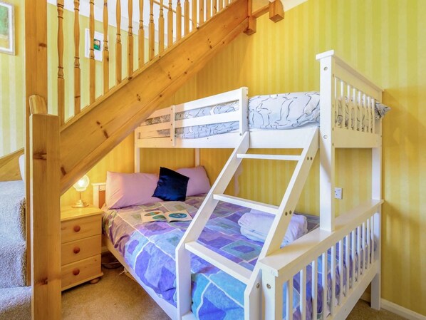 Una cama litera con escalera de madera y una mesita de noche con lámpara.