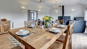 A dining area with a wooden table set for six, a chandelier, and a large window with curtains. - 2 Bed in South Molton (oc-88993) (Bishops Nympton)