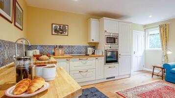 A modern kitchen with white cabinets, a microwave, oven, and a coffee maker. There is a wooden countertop with bread and a plate of croissants.