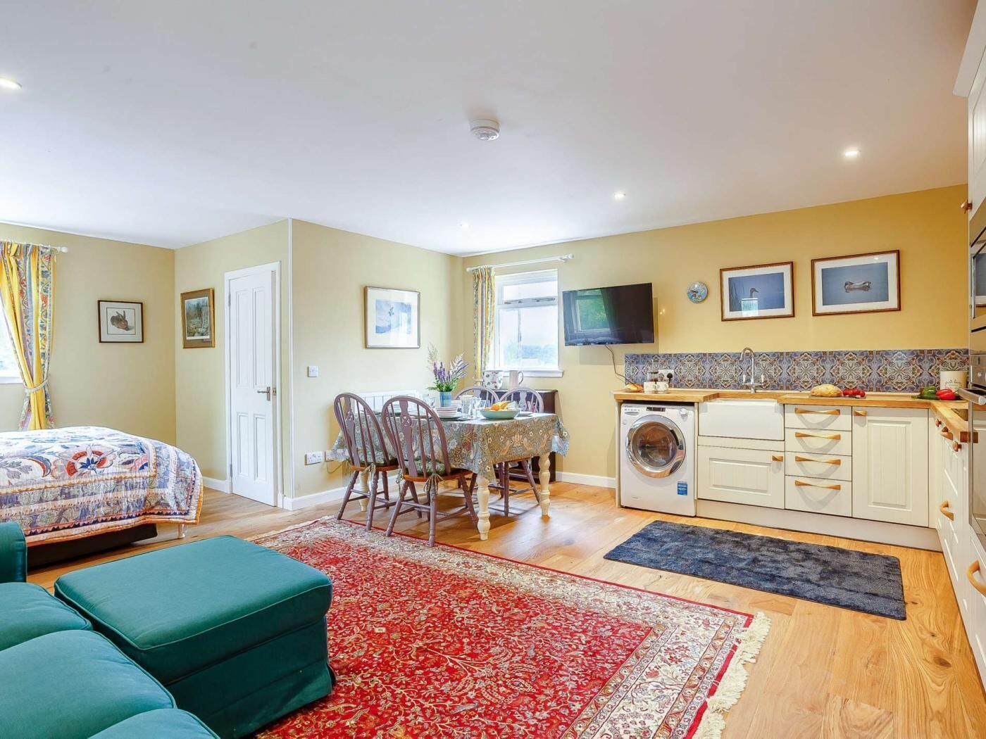 A compact living space with a bed, a dining area, a kitchen, and a washing machine.
