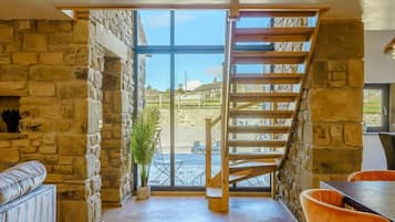 A room with a stone wall, a wooden staircase, a sofa, and a table.