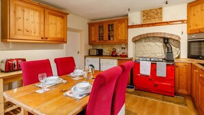 A compact kitchen with wooden cabinets, a red stove, and a dining table set for four. - 2 Bed in Hexham (oc-89086) (Redesmouth)