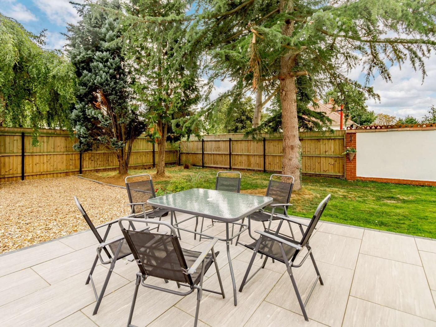 Une terrasse extérieure avec une table et des chaises, entourée d’une clôture en bois et d’arbres.
