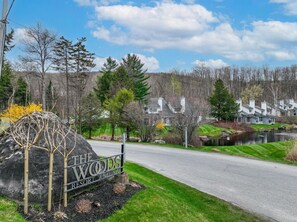 A sign for The Woods Resort, a paved road, and a body of water. - Pool, Hot Tub, Spa & Ski Shuttle (Killington)