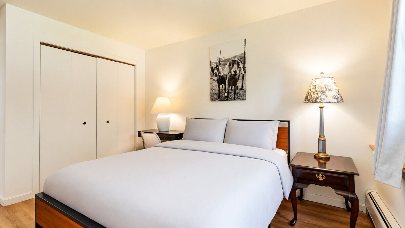 A hotel room with a bed, bedside tables, a lamp, a wall-mounted picture, and a door.