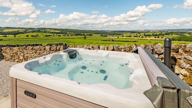 Un bain à remous avec un mur en pierre et une vue sur des champs et des collines verdoyants.