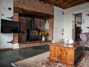 A living room with a brick fireplace, a television, a wooden coffee table, and a patterned rug. - 2 Bed in Norwich (oc-89598) (Haddiscoe)