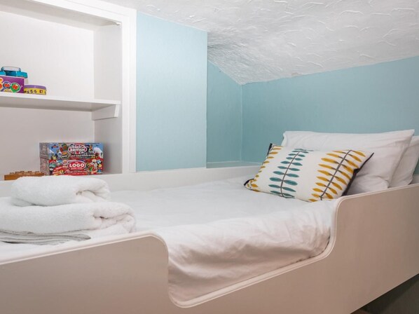 A single bed with white bedding, a shelf with children's toys, and a box of board games. - 2 Bed in Norwich (oc-89598) (Haddiscoe)