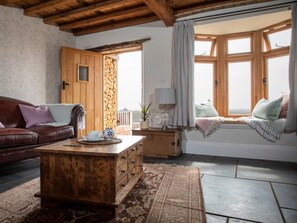 A cozy living room with a wooden coffee table, a leather sofa, a stone pillar, and a window with curtains. - 2 Bed in Norwich (oc-89598) (Haddiscoe)