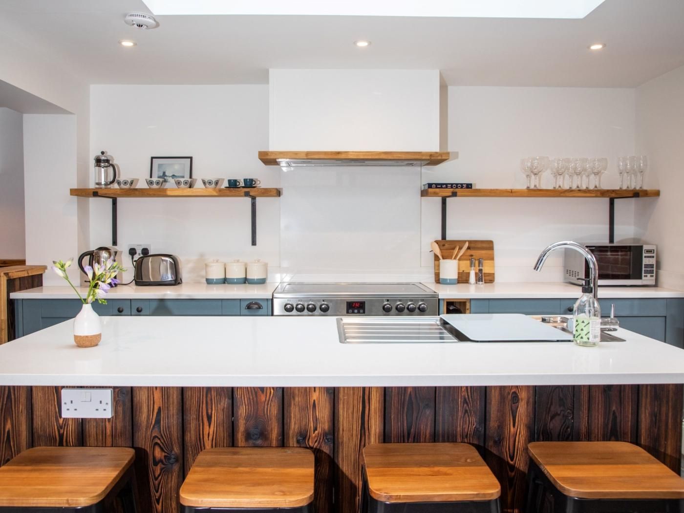 A modern kitchen with a central island, wooden stools, and a microwave.