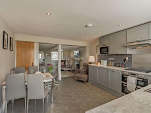 A modern kitchen with grey cabinets, a microwave, and a stove. There is a dining area with a table and chairs. - 2 Bed in Grange-over-sands (oc-89206) (Cartmel)