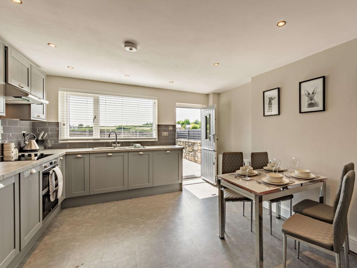 A modern kitchen with grey cabinets, a dining area with a table set for four, and a view through the window.