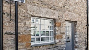 A stone building with a window and a door, a sign above the door, and a black pipe on the left. - 2 Bed in Grange-over-sands (oc-89206) (Cartmel)