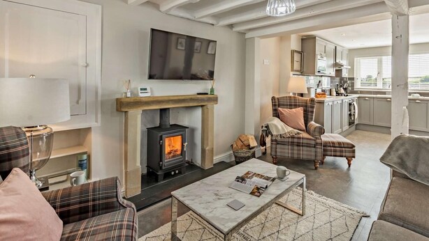 A living room with a fireplace, a television, and a kitchen in the background. - 2 Bed in Grange-over-sands (oc-89206) (Cartmel)