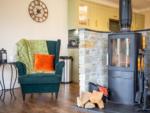 A cozy living room with a green armchair, a coffee table, and a fireplace with logs. - 3 Bed in Bideford (oc-89869) (Westward Ho!)