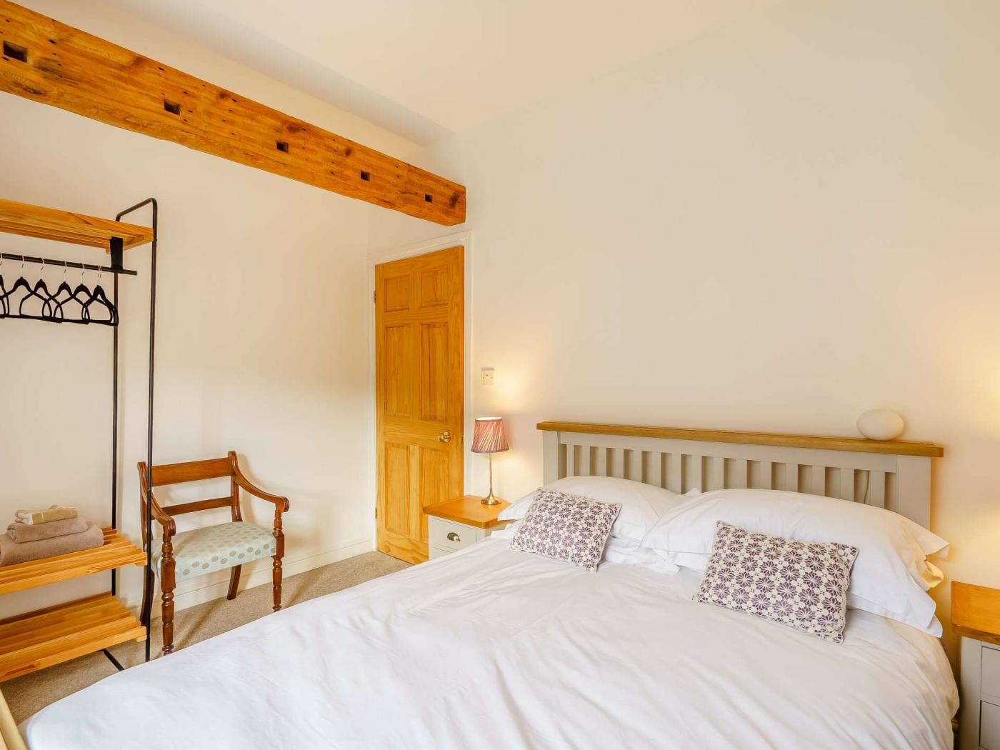 A bedroom with a wooden headboard, a bed with white bedding, a wooden chair, a wooden shelf, and a wooden wardrobe.
