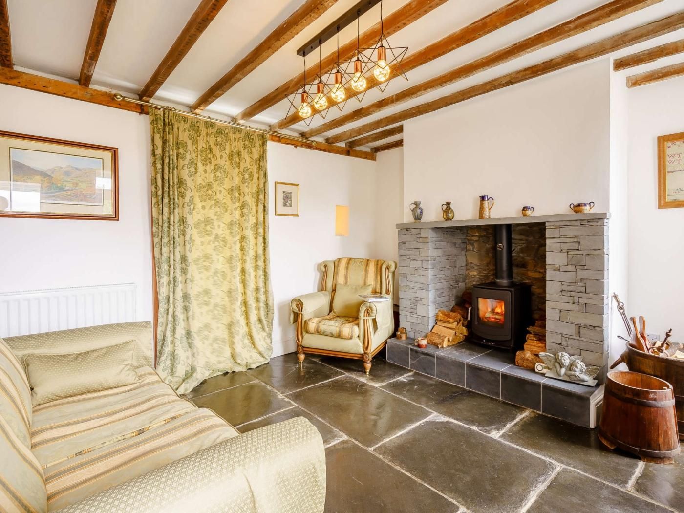 A cozy living room with a stone fireplace, a sofa, a patterned curtain, and a wooden ceiling.